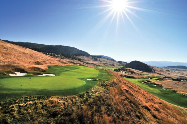 A golf course with a clear sky and sun, surrounded by hills and sparse vegetation. - Holiday Inn Express & Suites Kelowna - East by IHG (Kelowna)