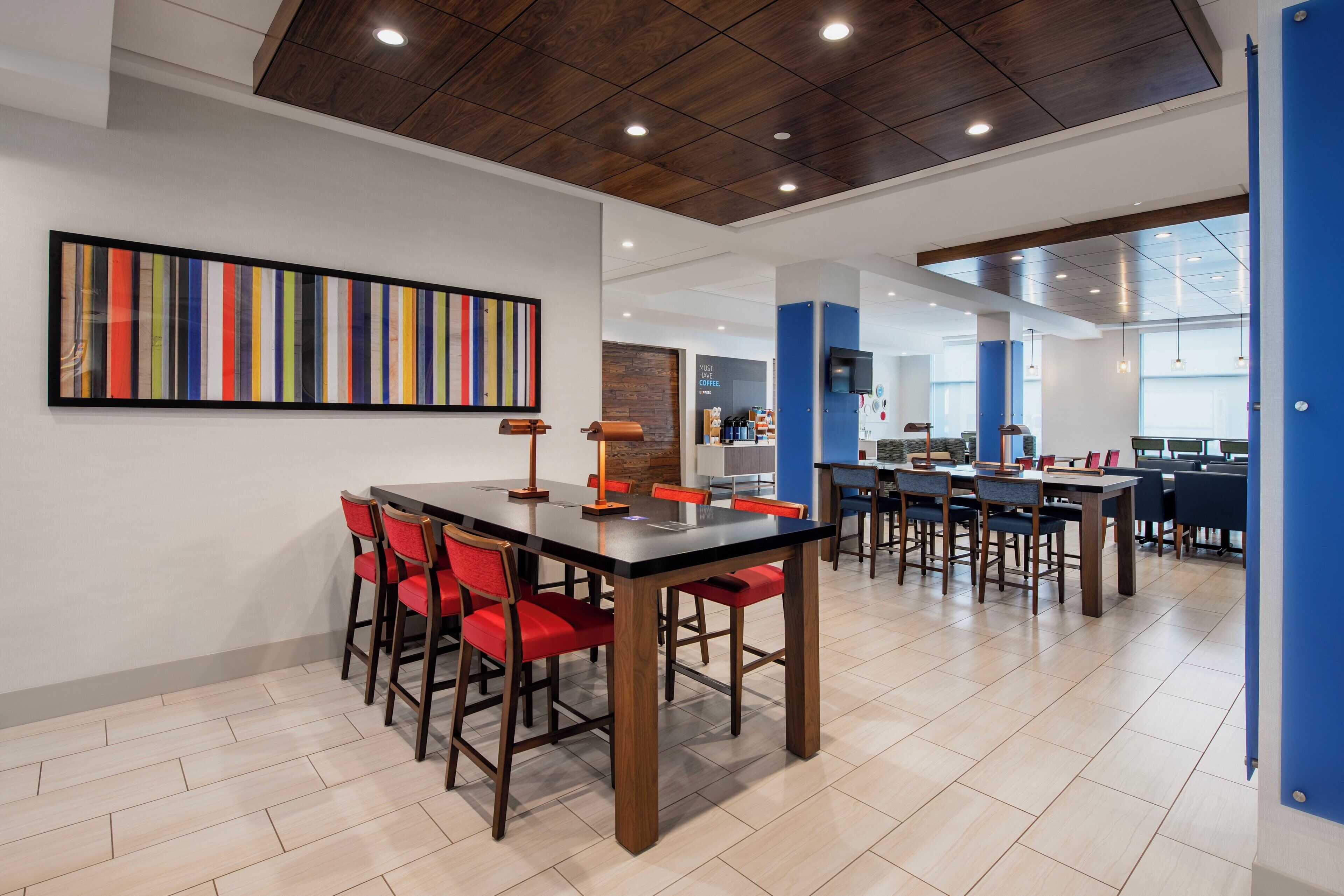 Un espace repas moderne avec une longue table, des chaises rouges et un tableau abstrait aux couleurs vives accroché au mur.