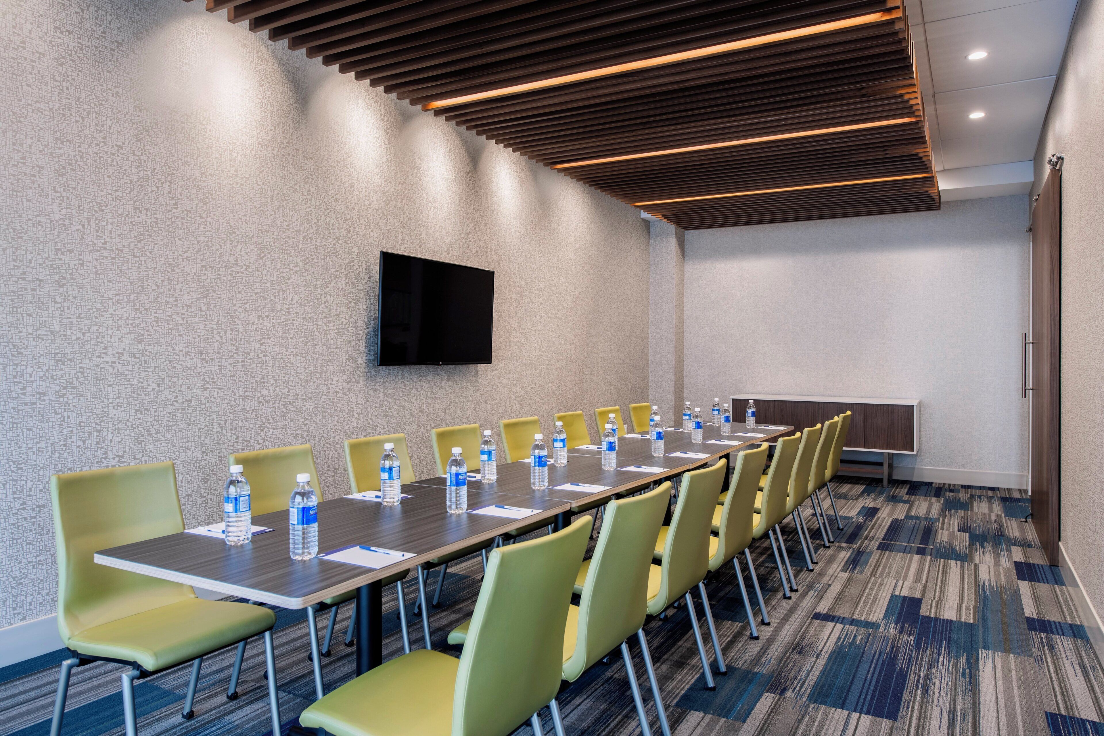 A conference room with a long table, chairs, water bottles, and a flat-screen TV on the wall.