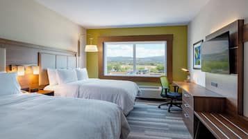 A hotel room with two beds, a desk, a chair, a TV, and a window with a view of a cityscape.