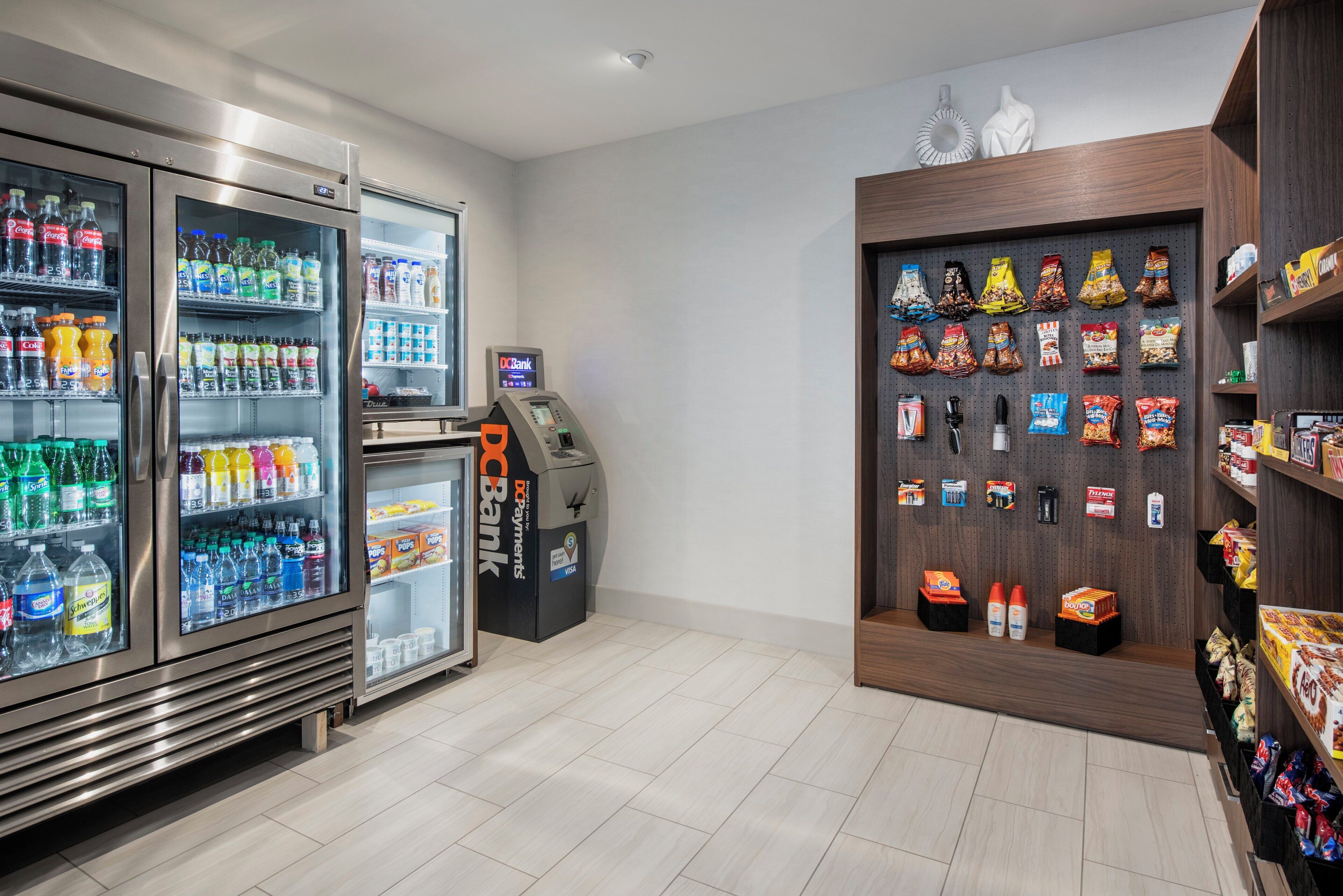 A self-service area with refrigerated beverage dispensers, a payment terminal, and snack vending machines.