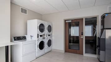 Une buanderie équipée de machines à laver et de sèche-linge superposés, d’un panneau de commande et d’un réfrigérateur.