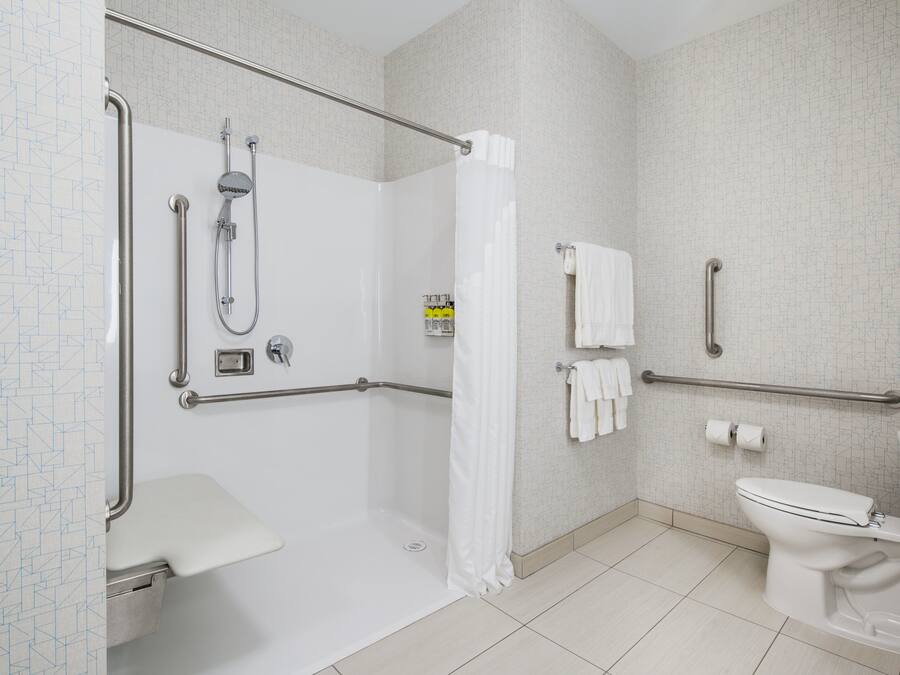 A modern bathroom with a shower, toilet, and sink. It includes grab bars and a wheelchair-accessible shower.