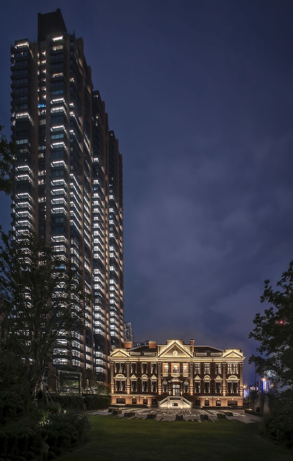A high-rise building with illuminated windows and a classical building with a central entrance and steps in front. - Bulgari Hotel Shanghai (Shanghai)