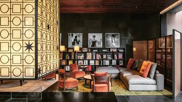 A modern lounge area with a geometric patterned wall, a sofa, armchairs, a coffee table, and a bookshelf with framed pictures.