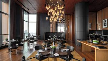 A modern dining area with round tables, black chairs, and a central chandelier.