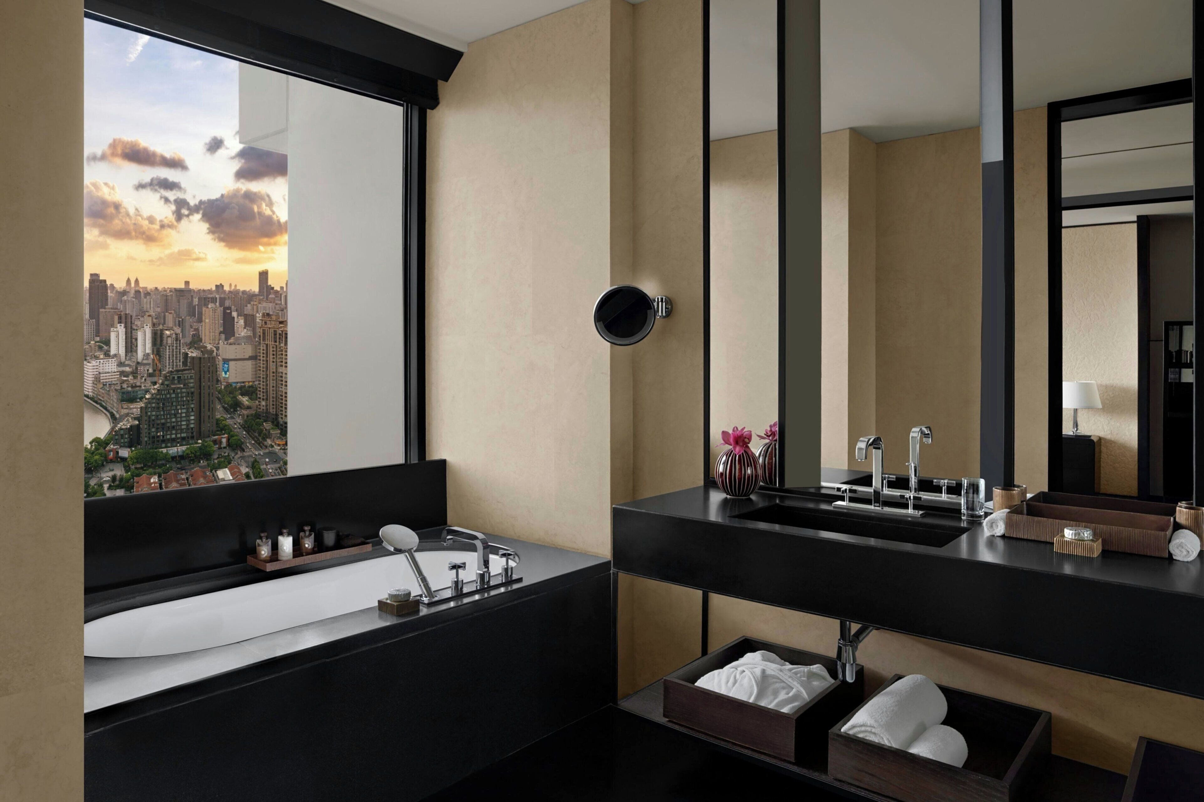 A modern bathroom with a large window, a black sink, and a mirror.