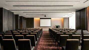 A conference room with rows of chairs, a projector screen, and a carpeted floor.