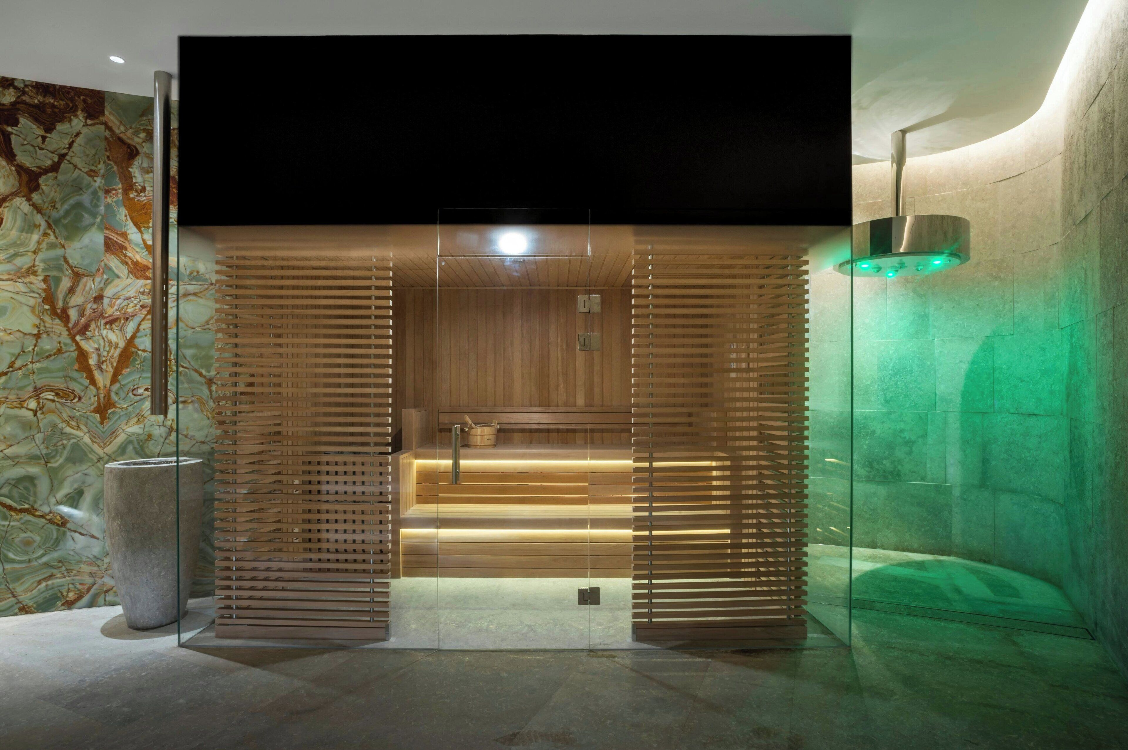 Een moderne spa-ingang met een houten paneeldeur, een stenen wasbak en een wand met groene verlichting.