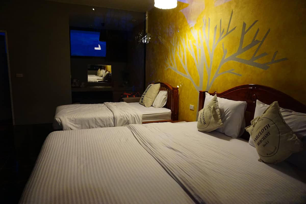 A hotel room with two beds, each with white linens and matching pillows. There is a wall-mounted TV and a tree decal on the wall.