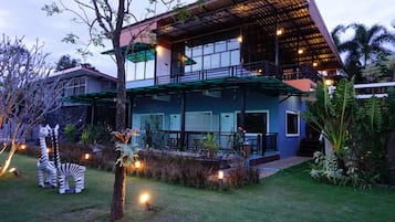 A two-story building with a balcony, surrounded by a well-maintained garden with decorative zebra statues and string lights.