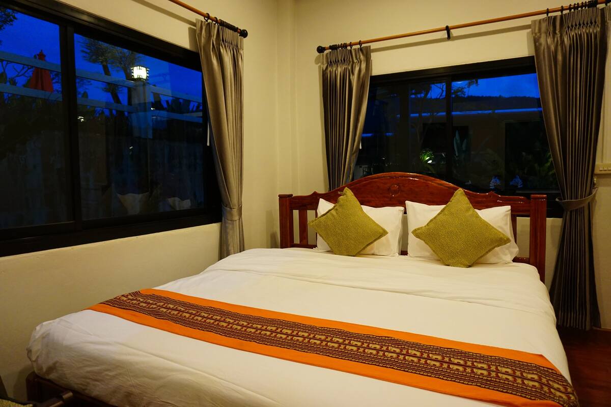 A neatly made bed with a white and orange bedspread, two green pillows, and a wooden headboard.