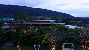 Un resort con un edificio grande, abundante vegetación y montañas al fondo.