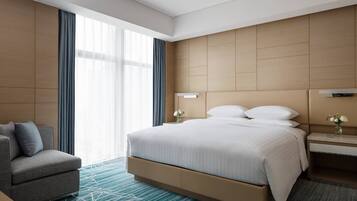 A modern hotel room with a large bed, a sofa, a nightstand, and a window with curtains.