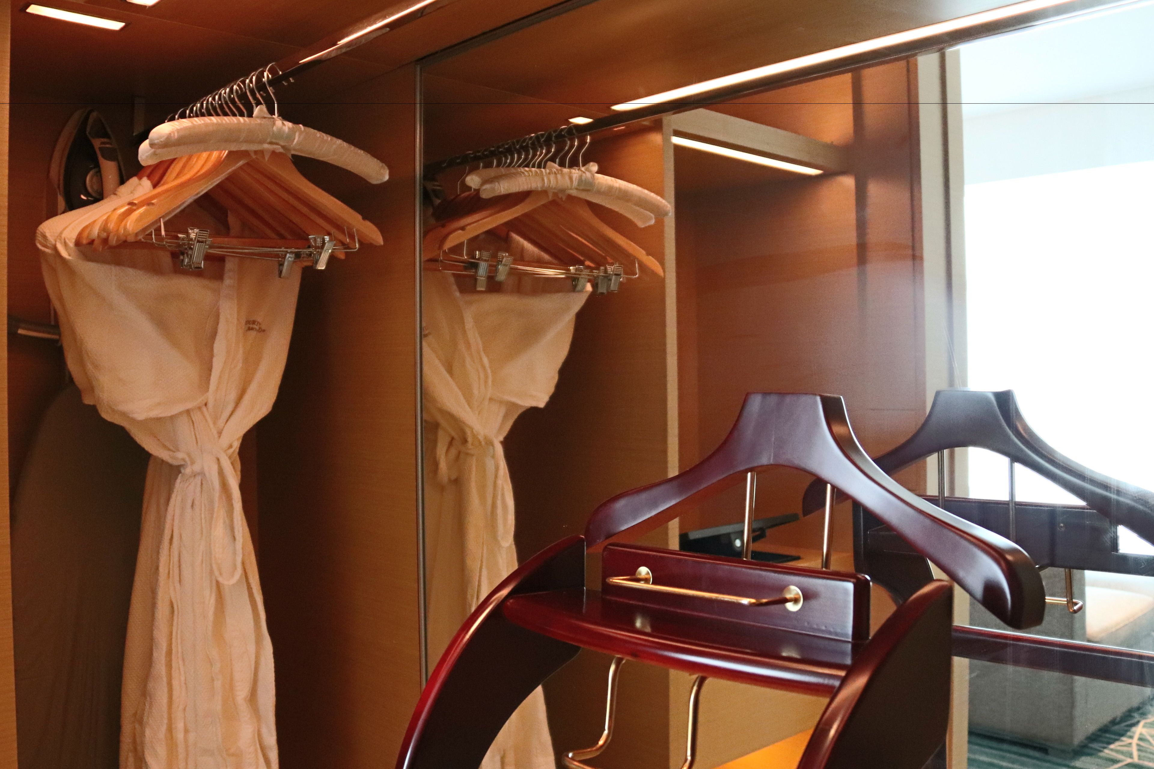A hotel room with a mirror reflecting a wooden chair and a rack of white robes.