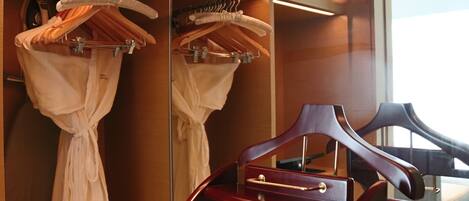 Une chambre d’hôtel avec un miroir dans lequel se reflète une chaise en bois et un portant rempli de peignoirs blancs.