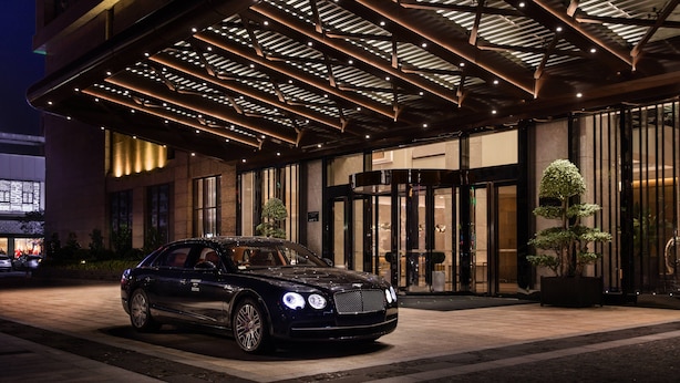A luxury hotel entrance with a black car parked in front, a covered entrance area, and a large potted tree. - Courtyard by Marriott Shunde Longjiang (Foshan)