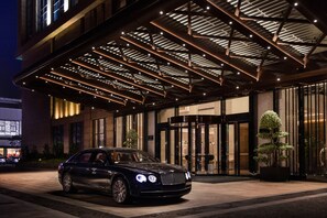 A luxury hotel entrance with a black car parked in front, a covered entrance area, and a large potted tree. - Courtyard by Marriott Shunde Longjiang (Foshan)