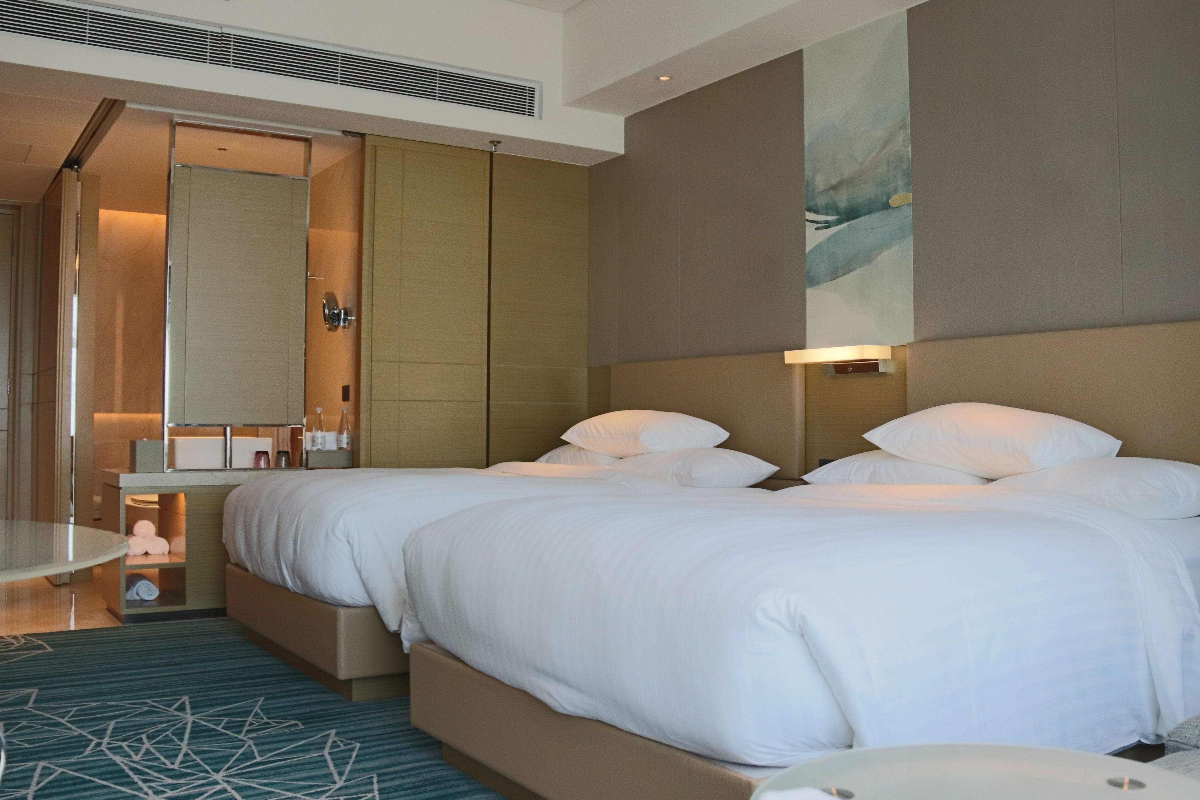 A hotel room with two beds, a bathroom, and a large painting on the wall.