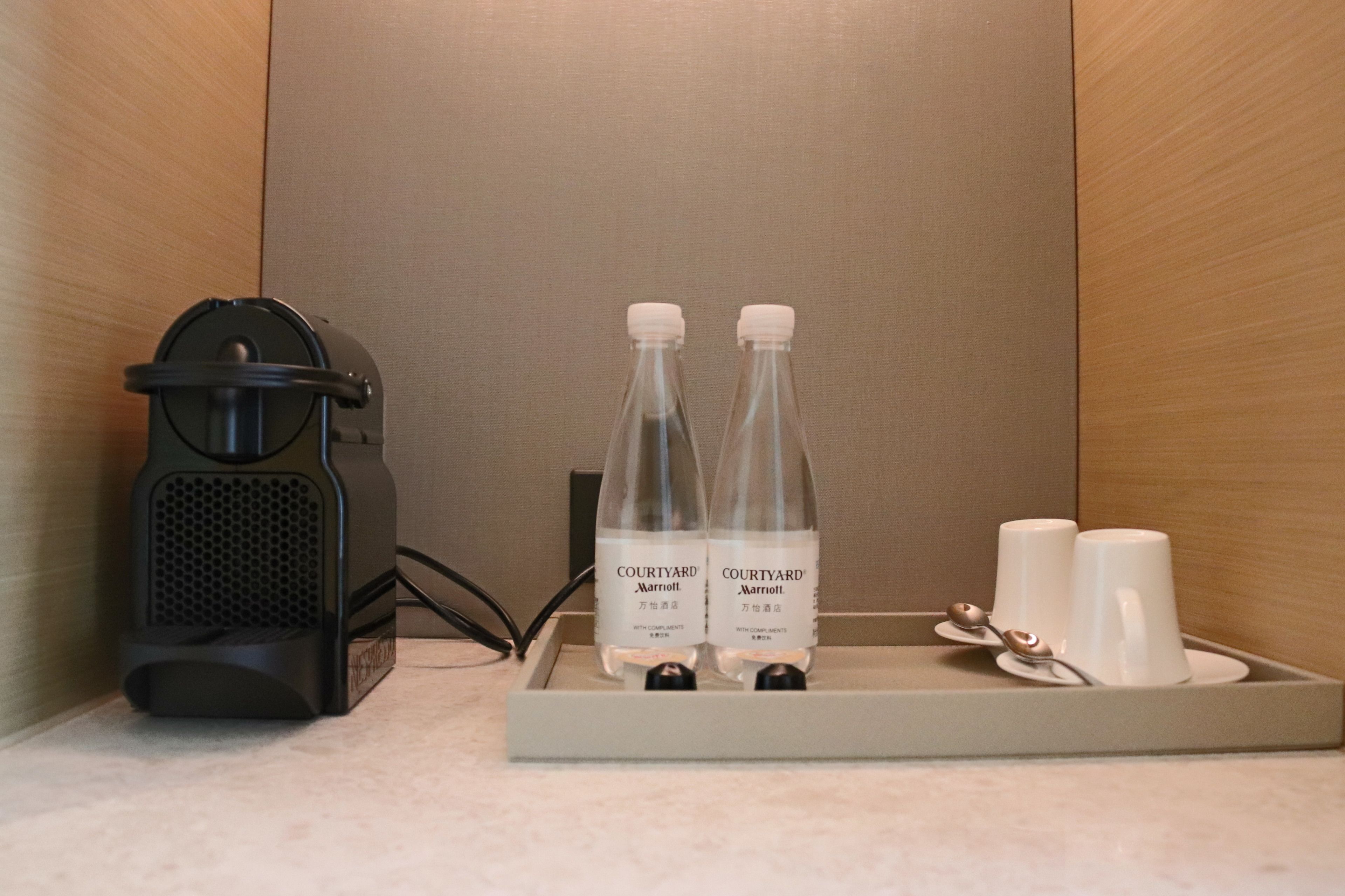 Un plateau contenant deux bouteilles d’eau de la marque Courtyard Marriott, deux tasses blanches et un appareil noir, vraisemblablement une machine à café, posé sur un comptoir.