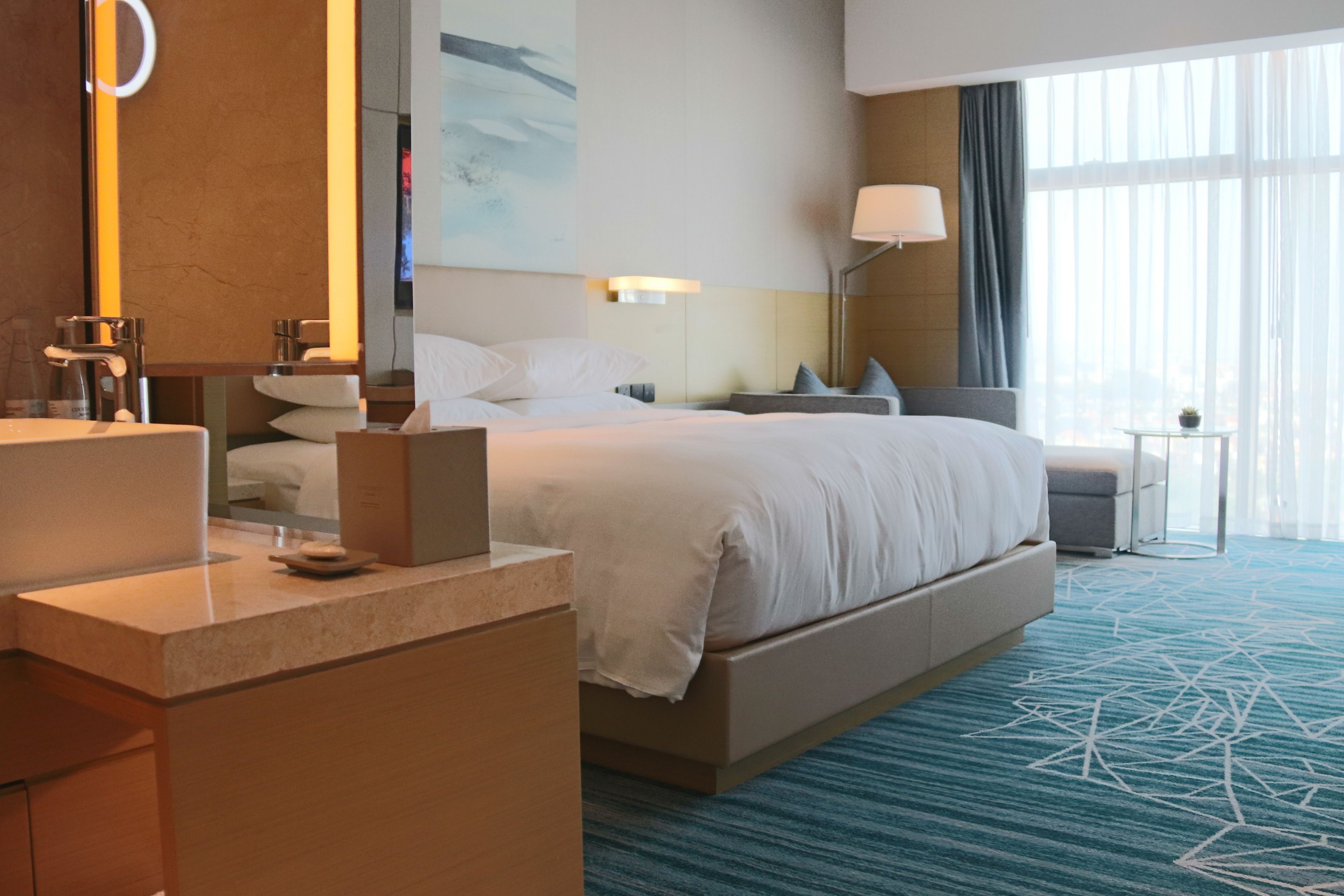 Une chambre d’hôtel avec un grand lit, un bureau avec une chaise, une petite table et une grande fenêtre avec des rideaux.
