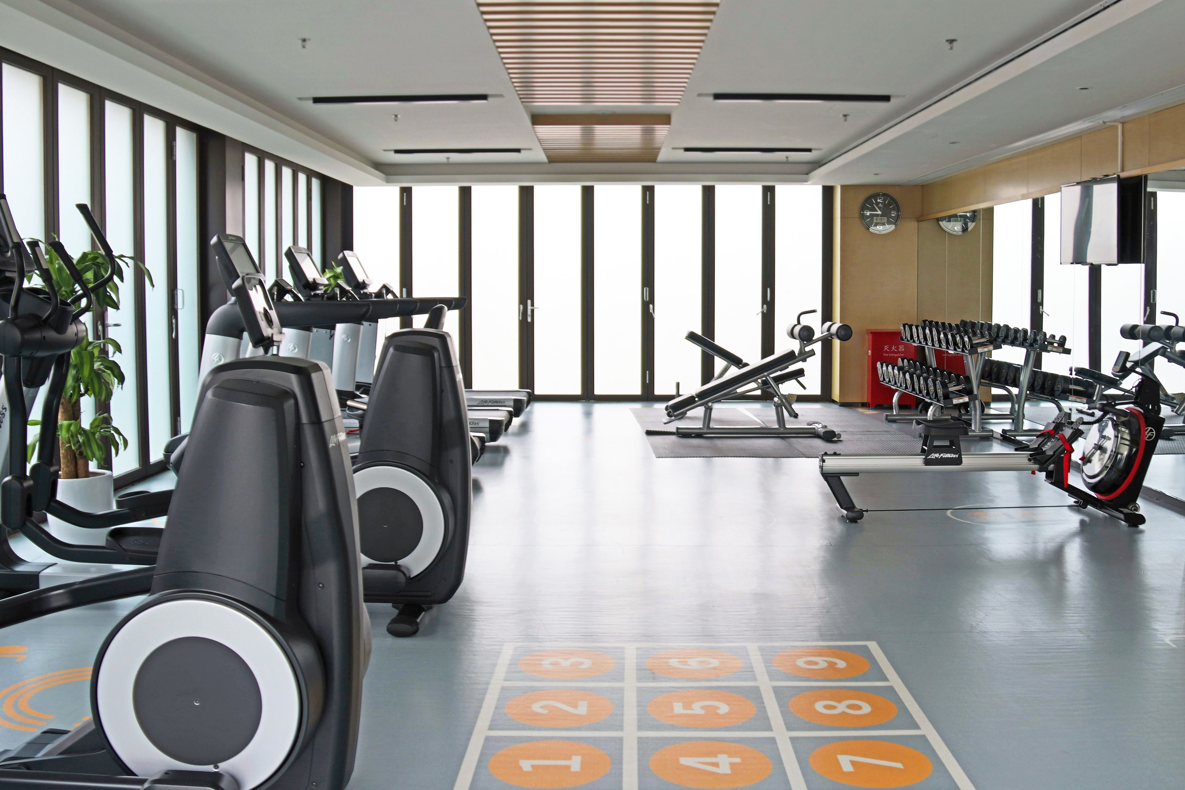 Une salle de sport équipée de matériel d’exercice, dotée de grandes fenêtres et d’un sol recouvert de carreaux numérotés.