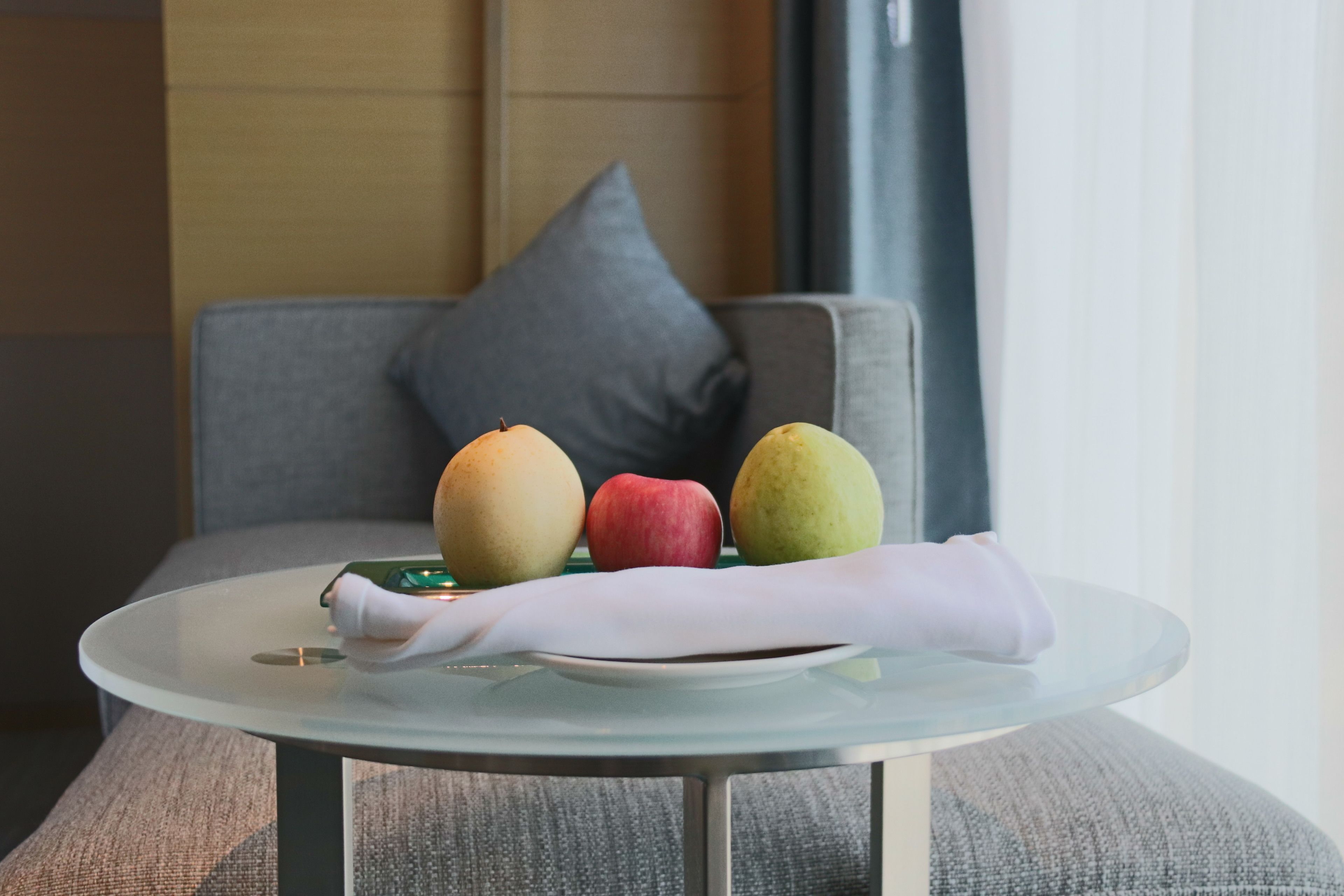 A round glass table with a plate of fruit and a wrapped item.