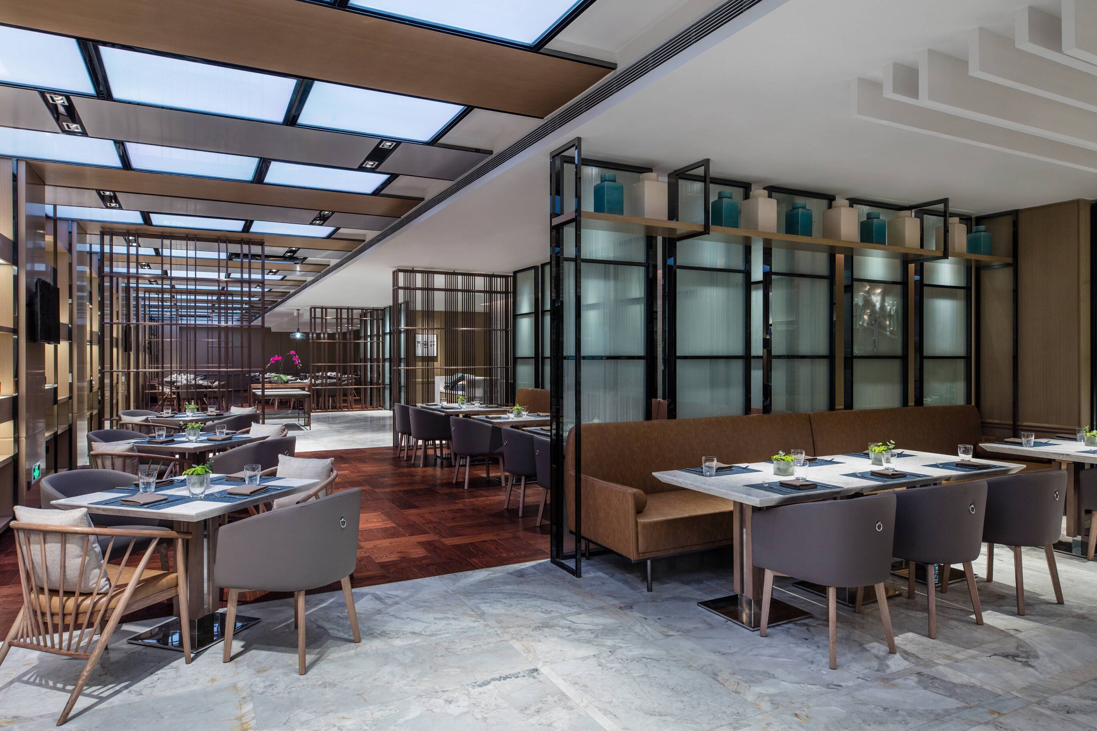 A modern restaurant with a high ceiling, skylights, and a mix of seating arrangements including tables and booths.