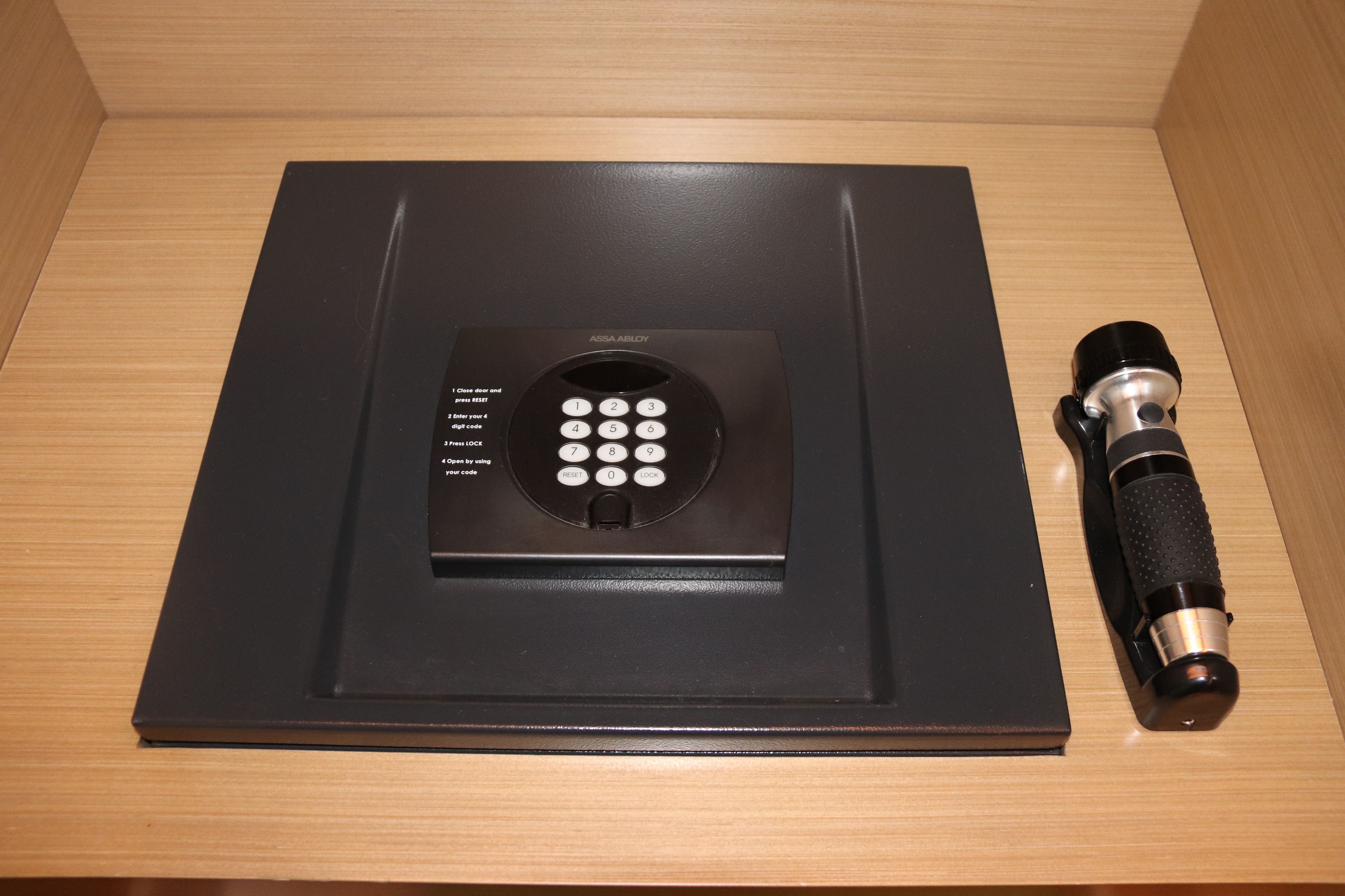 Un dispositivo electrónico negro con teclado y una linterna sobre una superficie de madera.