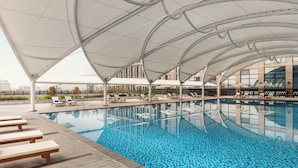 A swimming pool with a canopy overhead, lounge chairs, and a building in the background. - Courtyard by Marriott Shunde Longjiang (Foshan)
