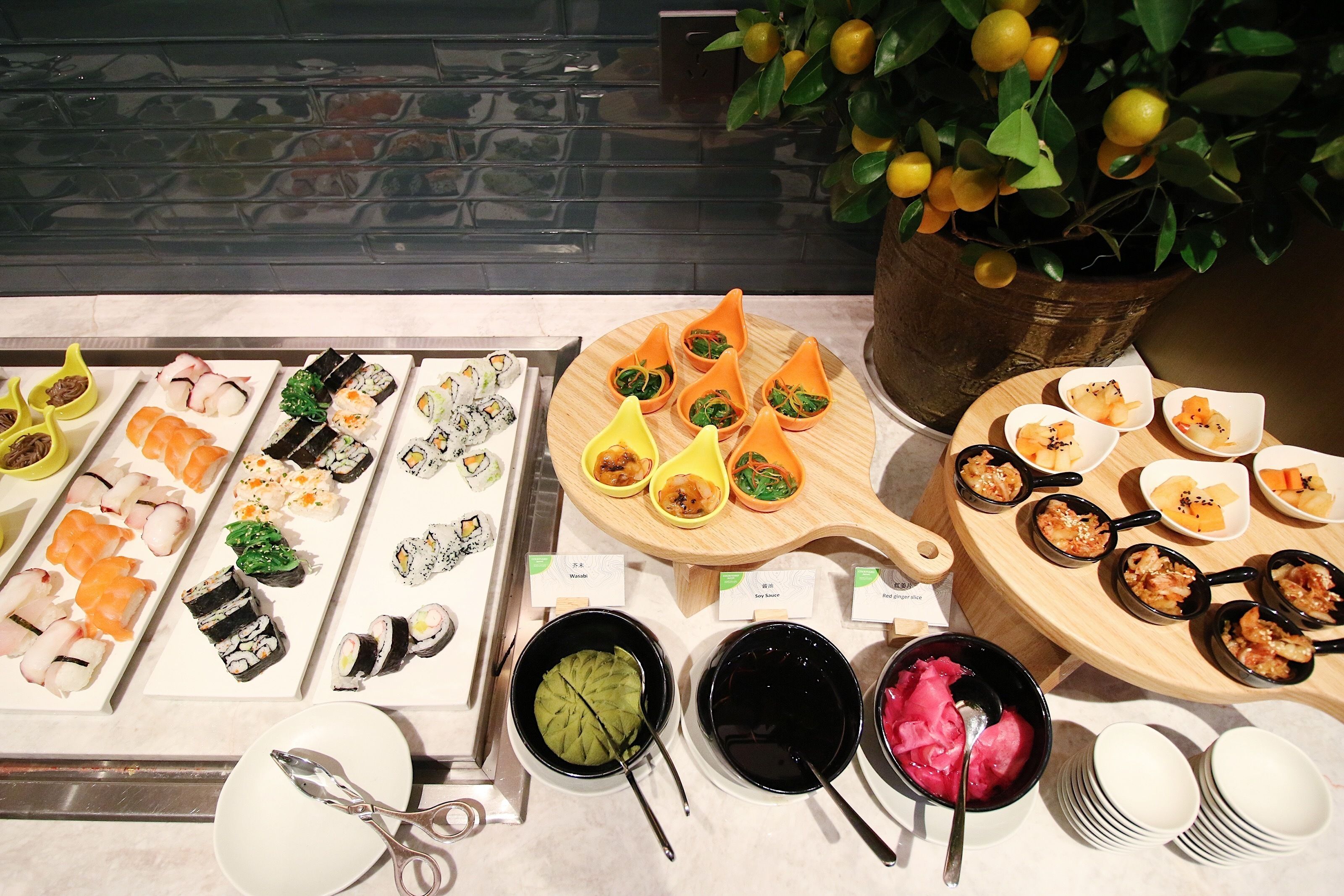 Un buffet proposant une variété de plats, dont des sushis, disposés sur une table, avec une plante en pot en arrière-plan.