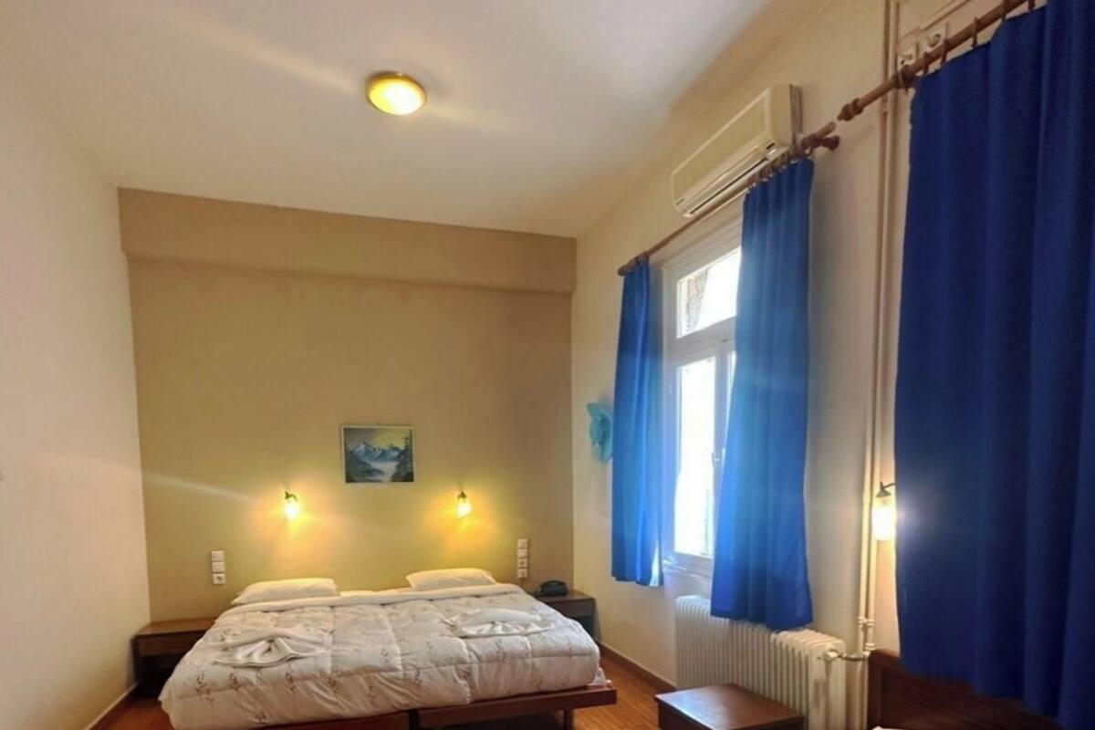 A hotel room with two beds, wooden flooring, a window with blue curtains, and wall-mounted lights.