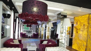 A modern hotel lobby with plush seating, a large decorative column, and a vibrant yellow accent wall. - Harmony Palace (Burgas)
