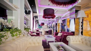 A spacious lounge area with plush seating, a central coffee table, and decorative elements like hanging lamps and plants. - Harmony Palace (Burgas)