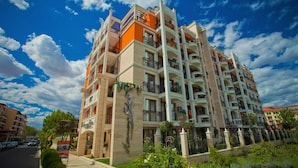 A multi-story residential building with balconies, a visible storefront, and a clear sky. - Harmony Palace (Burgas)