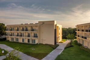 A modern multi-story hotel with a flat facade, multiple balconies, and a well-maintained lawn area. - Eastin Thana City Golf Resort (Bangkok Noi)