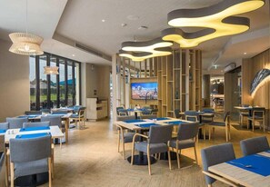 A modern dining area with tables and chairs, a large screen, and a view of the outdoors. - Eastin Thana City Golf Resort (Bangkok Noi)