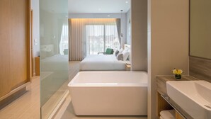 Una habitación de hotel moderna con una bañera grande, una cama con ropa blanca y vistas a la ciudad a través de amplios ventanales.