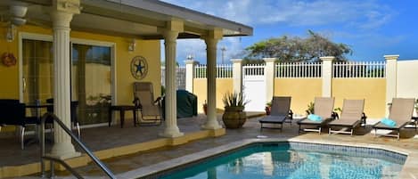A pool area with lounge chairs, a covered seating area, and a clock on the wall.