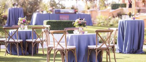 An outdoor seating area with tables covered in blue tablecloths and wooden chairs.