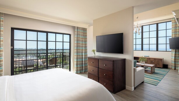 A hotel room with a large bed, a TV mounted on the wall, a balcony with a view, and a seating area with a table and chairs. - Westin Carlsbad Resort & Spa (Carlsbad)