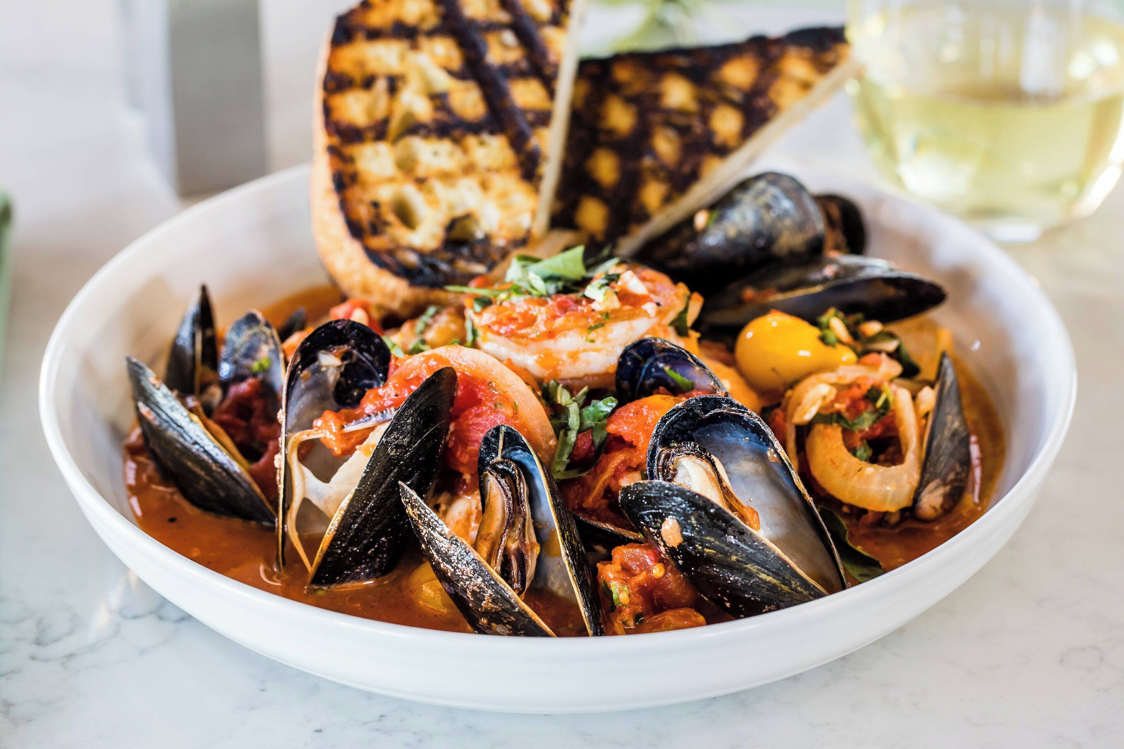 A bowl of seafood stew with mussels and shrimp, served with toasted bread.