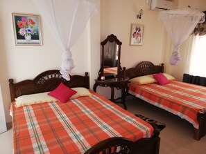 A room with two beds, each with a plaid bedspread and pillows, a wooden headboard, a bedside table, and a mirror. - Abha Villa (Galle)