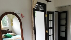 A bedroom with a bed, a wooden dresser, a mirror, and a door leading to another room. - Abha Villa (Galle)