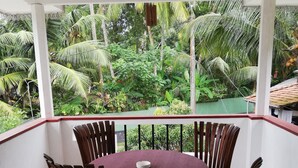 A covered outdoor dining area with a round table and chairs, surrounded by a white railing, overlooking a lush garden with various plants and trees. - Abha Villa (Galle)