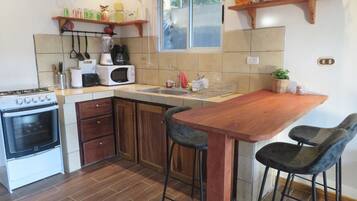 A kitchen with a stove, microwave, sink, wooden cabinets, and a wooden bar table with two chairs.