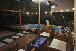 An outdoor patio area with a pool, wicker furniture, and string lights. - Villa Picasso (Cóbano)