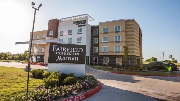 A Fairfield Inn & Suites Marriott hotel with a sign, a parking lot, and a landscaped area with flowers.