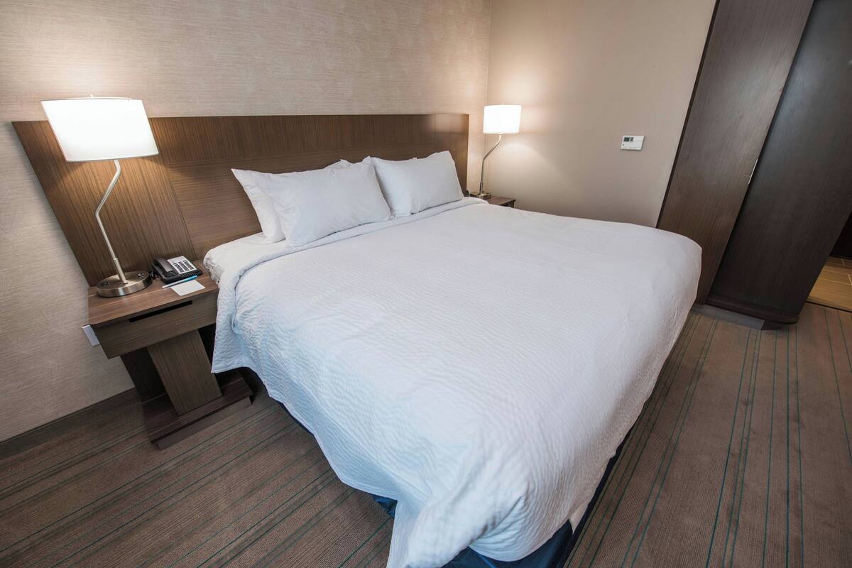 Ein Hotelzimmer mit einem großen Bett, zwei Nachttischlampen, einem Nachttisch mit Telefon und einem hölzernen Kopfteil.