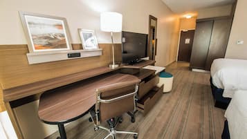 A hotel room with a wooden desk, a chair, a television, a bed, and a small round table.